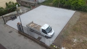Ein weißer Lastwagen steht auf einem Schotterplatz, in der Nähe ein Metallzaun und ein Motorrad.