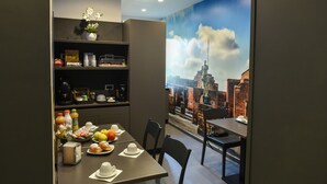 Ein Essbereich mit einem für das Frühstück gedecktem Tisch, einer Kaffeemaschine und einem Regal mit diversen Gegenständen.