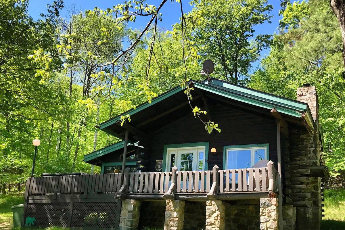 Une cabane rustique avec des fondations en pierre, un toit végétalisé et une terrasse en bois.