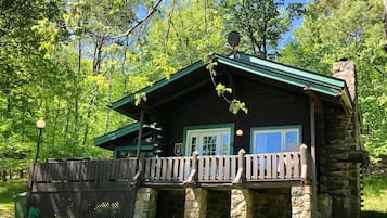 Une cabane rustique avec des fondations en pierre, un toit végétalisé et une terrasse en bois.