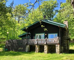 Uma cabana rústica com base de pedra, telhado verde e deck de madeira.