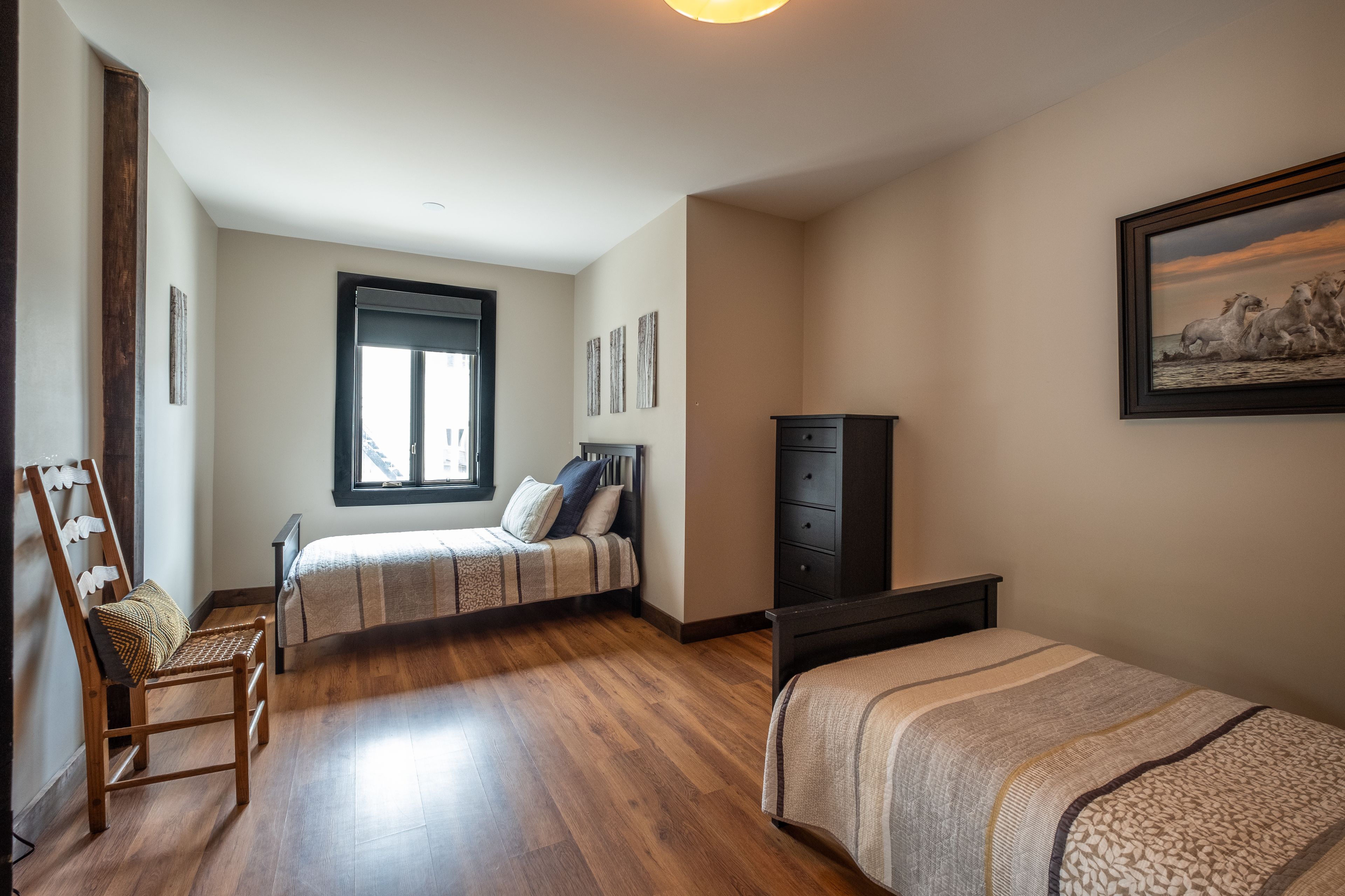 Een slaapkamer met twee bedden, een houten vloer, een raam en een schilderij aan de muur.