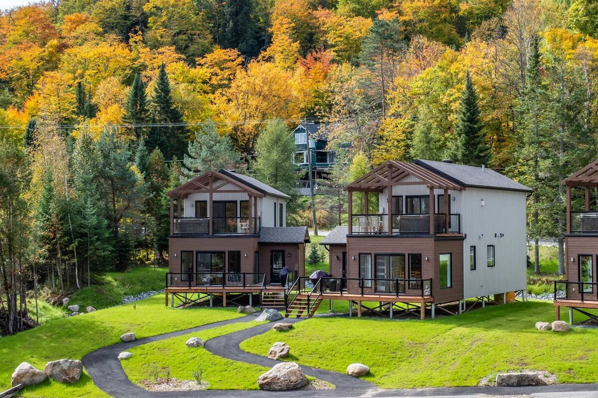 Un hôtel moderne de style chalet, avec des bâtiments à deux étages, des terrasses en bois et un chemin menant à l’entrée.