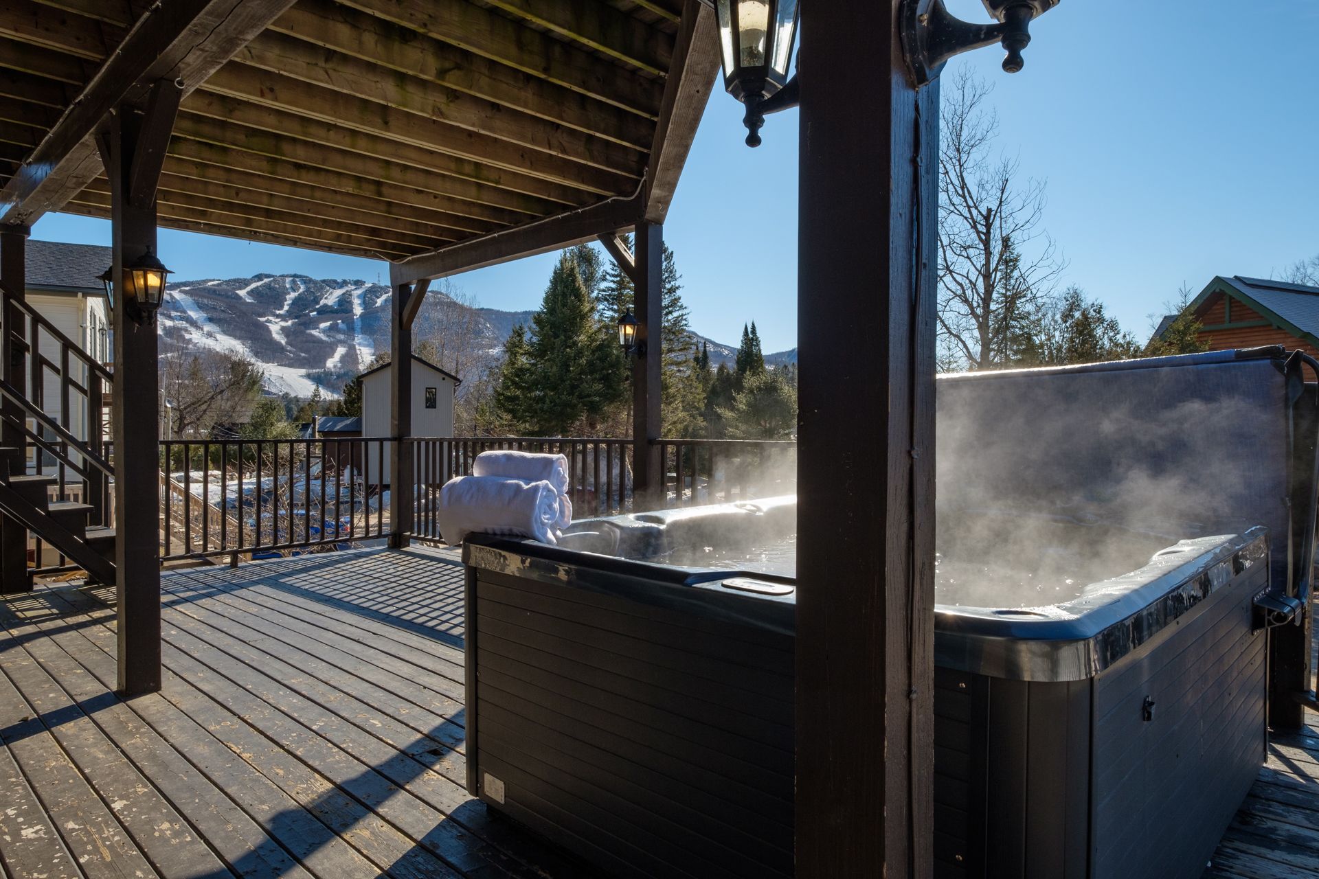 A wooden deck with a hot tub, a covered area with a railing, and a mountain view in the background.