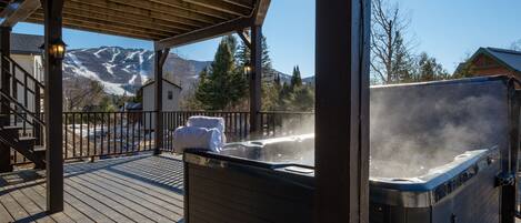 A wooden deck with a hot tub, a covered area with a railing, and a mountain view in the background.