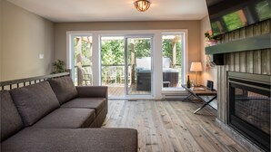 Un salon moderne avec un canapé d’angle, une cheminée et une porte-fenêtre coulissante donnant sur une terrasse extérieure.