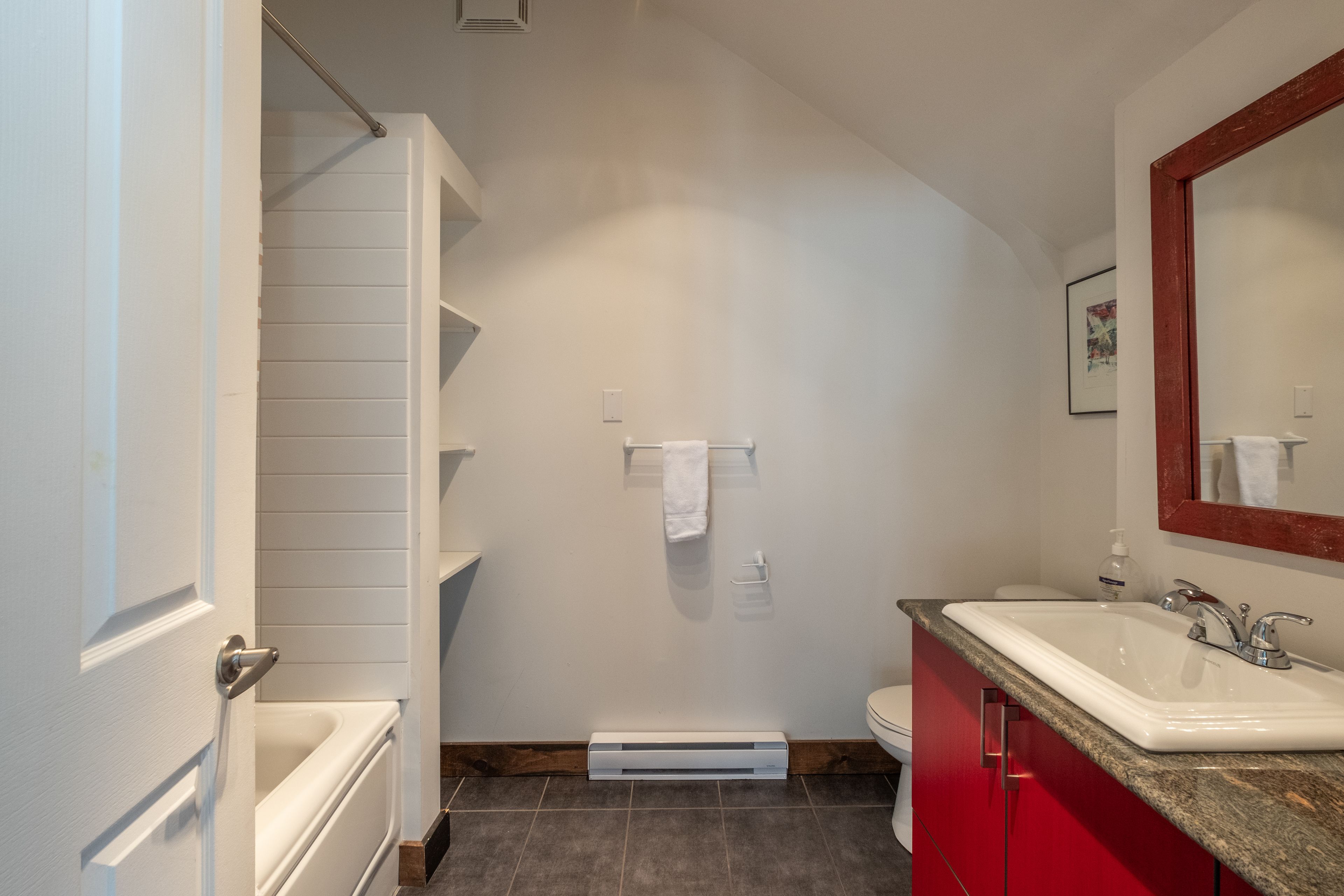 Une salle de bain avec une baignoire blanche, un meuble-lavabo rouge, un lavabo blanc et un miroir.