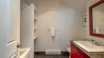 A bathroom with a white bathtub, a red vanity, a white sink, and a mirror.