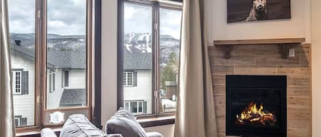 A living room with a fireplace, large windows, and a deer artwork.