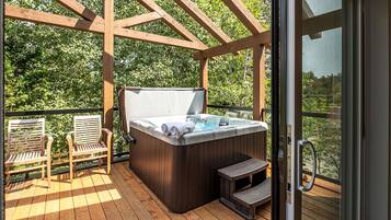 Un bain à remous sur une terrasse en bois, surmontée d’une pergola, le tout entouré de verdure.
