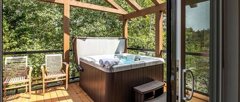 A hot tub on a wooden deck with a pergola overhead, surrounded by greenery.