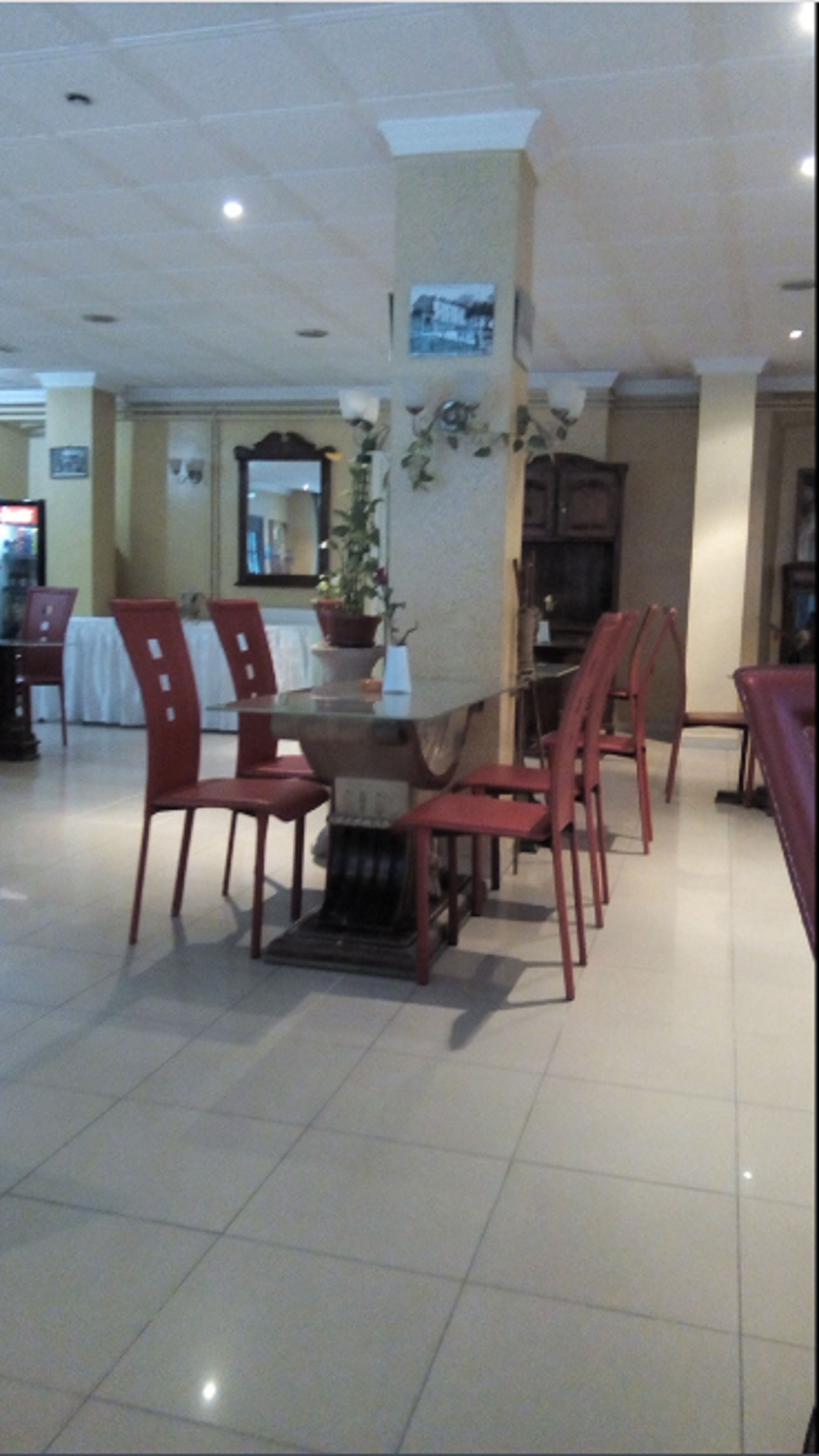 Un comedor con una mesa central rodeada de sillas rojas, una planta en maceta y un televisor sobre un mueble.