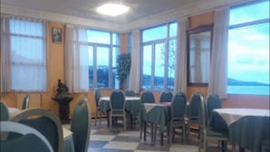 En matplats med rutmönstrat golv, bord med stolar, stora fönster med gardiner och utsikt över omgivningen.