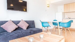 A modern living room with a grey sofa, two blue chairs, a wooden coffee table, and a flat-screen TV mounted on the wall. - Estudio A 20M Del Centro Cívico (San Carlos de Bariloche)