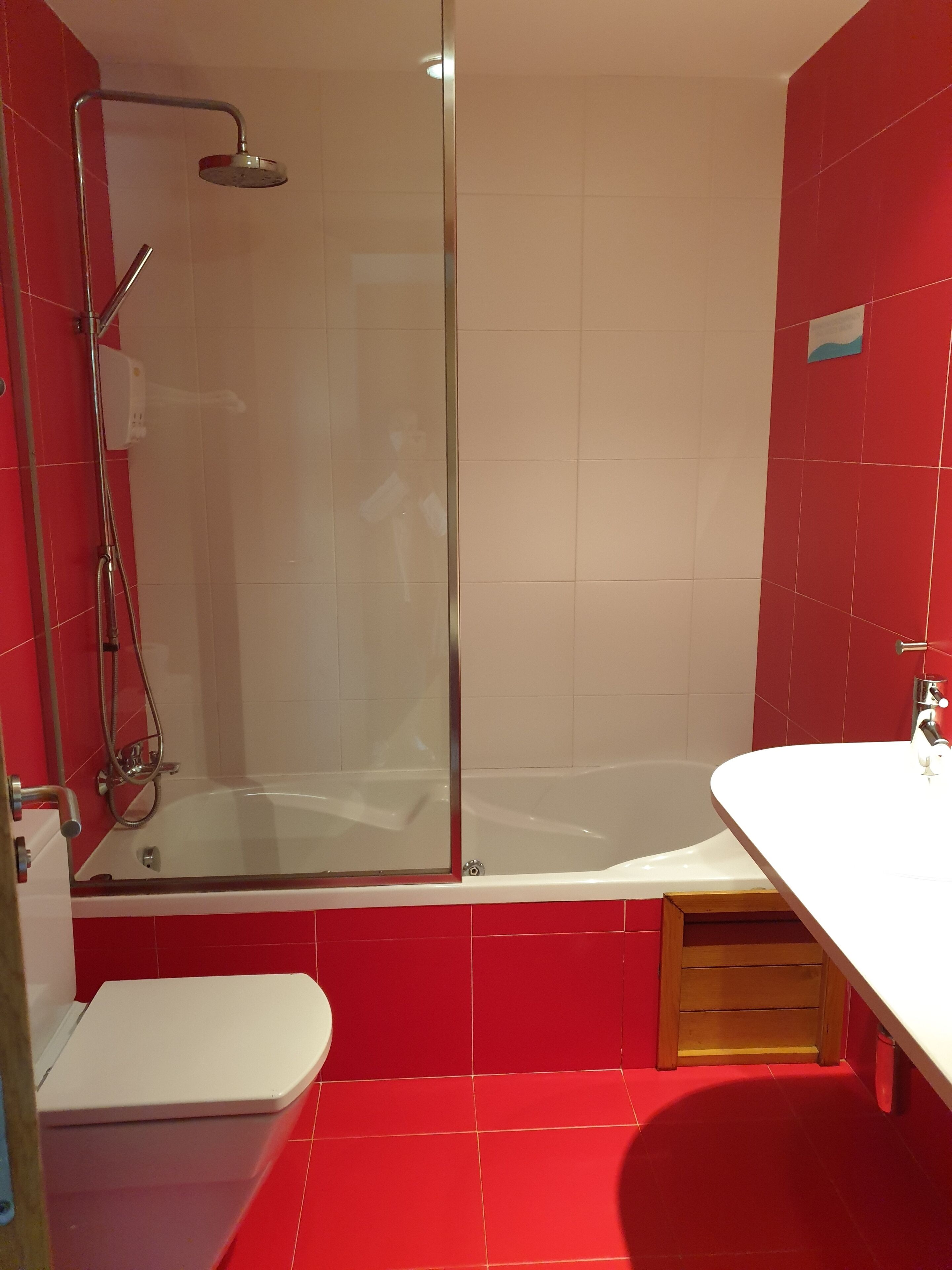 A modern bathroom with a glass-enclosed shower, a white bathtub, and a red-tiled floor.