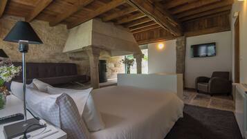A bedroom with a large bed, a bedside table with a lamp, a TV mounted on the wall, and a stone fireplace.