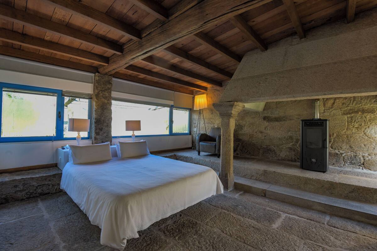 Une chambre avec un mur en pierre, un lit, une table de chevet, une lampe et une cheminée.