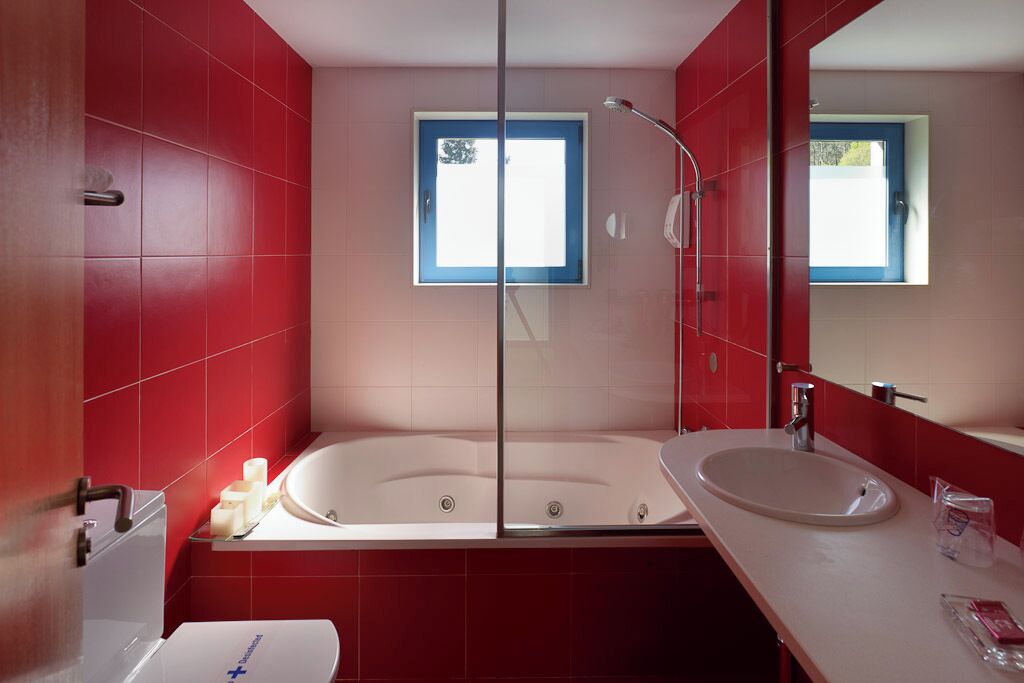 Ein modernes Badezimmer mit roten Fliesen, einer Duschkabine, einer weißen Badewanne und einem Waschbecken mit Spiegel.