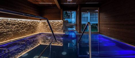 Un área de spa con pared de piedra, una bañera de hidromasaje con cerramiento de vidrio y paneles de madera.