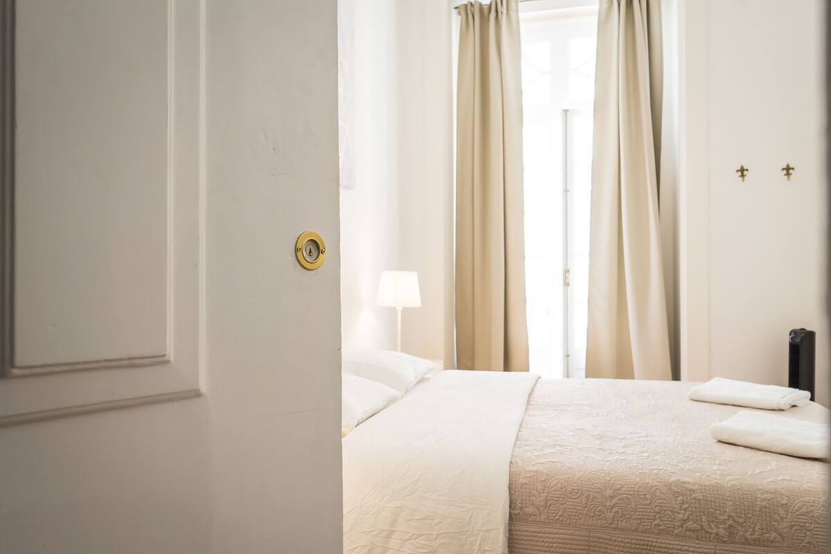 A hotel room with a bed, a nightstand, and a window with curtains.