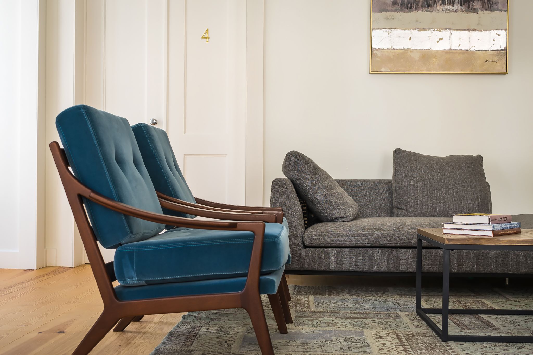 A living room with a blue chair, a grey sofa, and a coffee table with books.