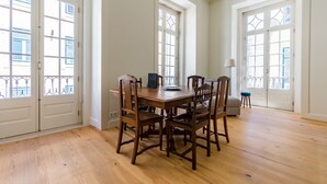 A dining area with a wooden table and chairs, large windows with decorative glass panes, and a view of the outside. - Santa Justa Prime Guesthouse (Lisbon)
