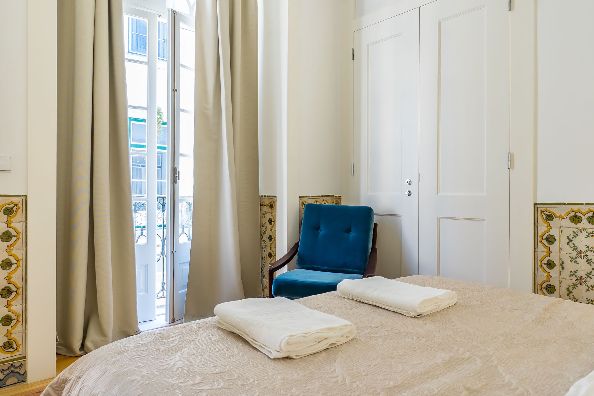 Een hotelkamer met een bed, een blauwe stoel en uitzicht op een gebouw door het raam.