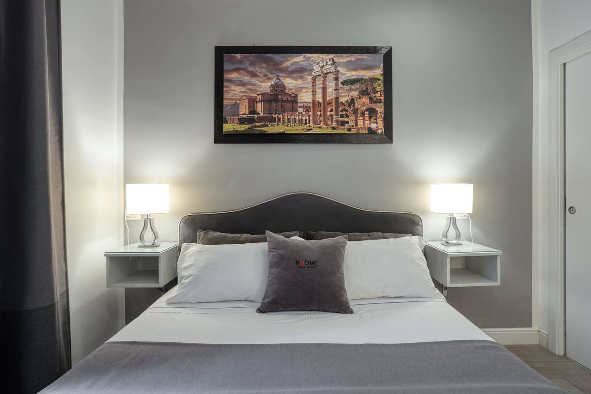 A neatly made bed with a pillow, two bedside lamps, and a framed picture of a historical building on the wall.