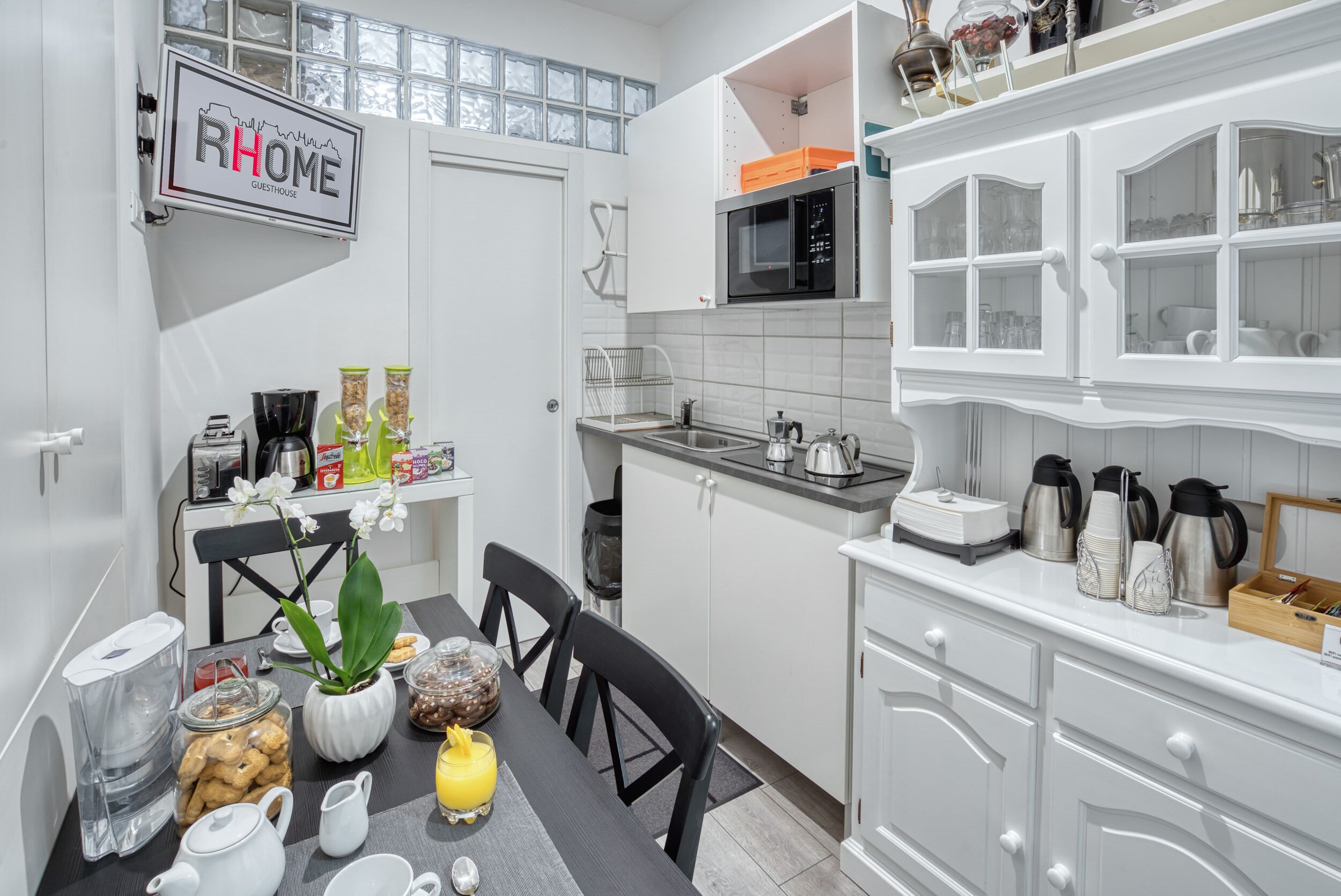 A modern kitchen with white cabinets, a microwave, and a coffee maker. There is a dining table with chairs and a vase of flowers.