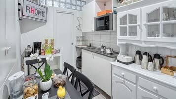 A modern kitchen with white cabinets, a microwave, and a coffee maker. There is a dining table with chairs and a vase of flowers.