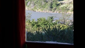 En vy över en flod med tät vegetation och kullar i bakgrunden.