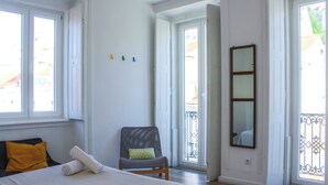 A bedroom with a bed, a chair, a window, and a door. - The Color Hostel (Lisbon)