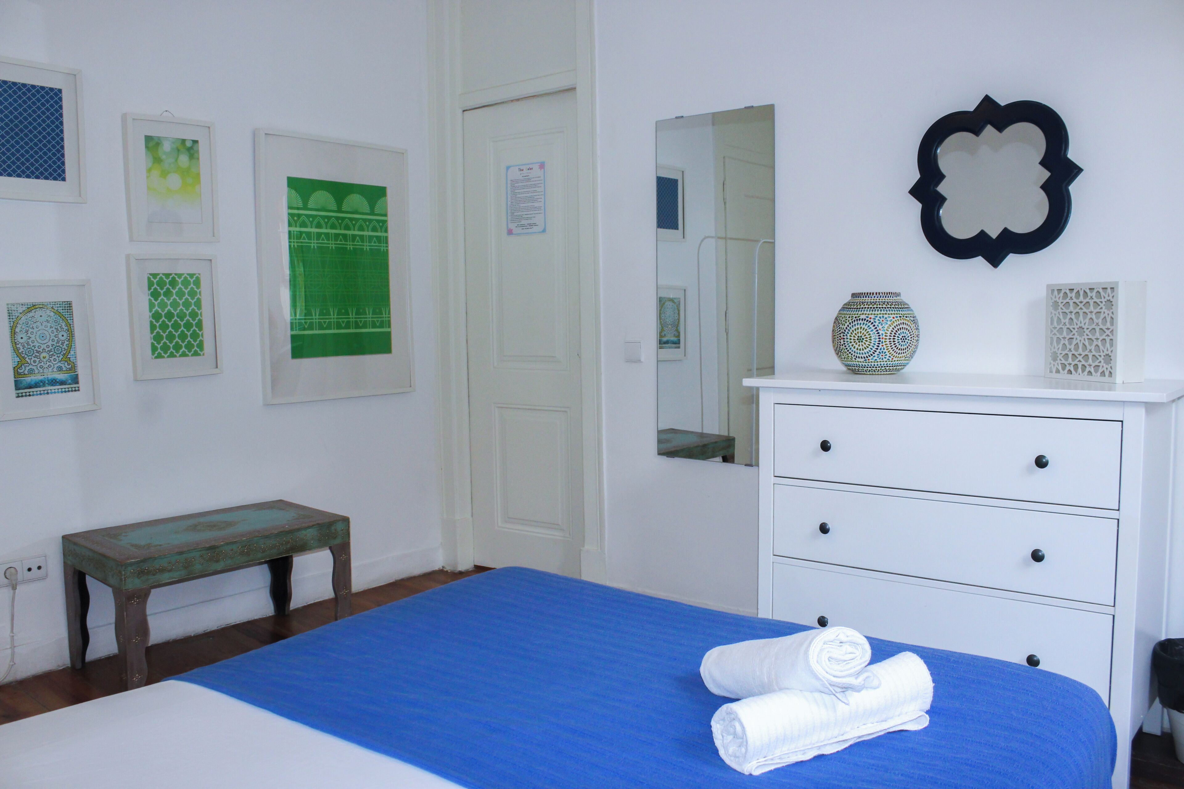 A bedroom with a bed, a dresser, a bench, and wall decorations.