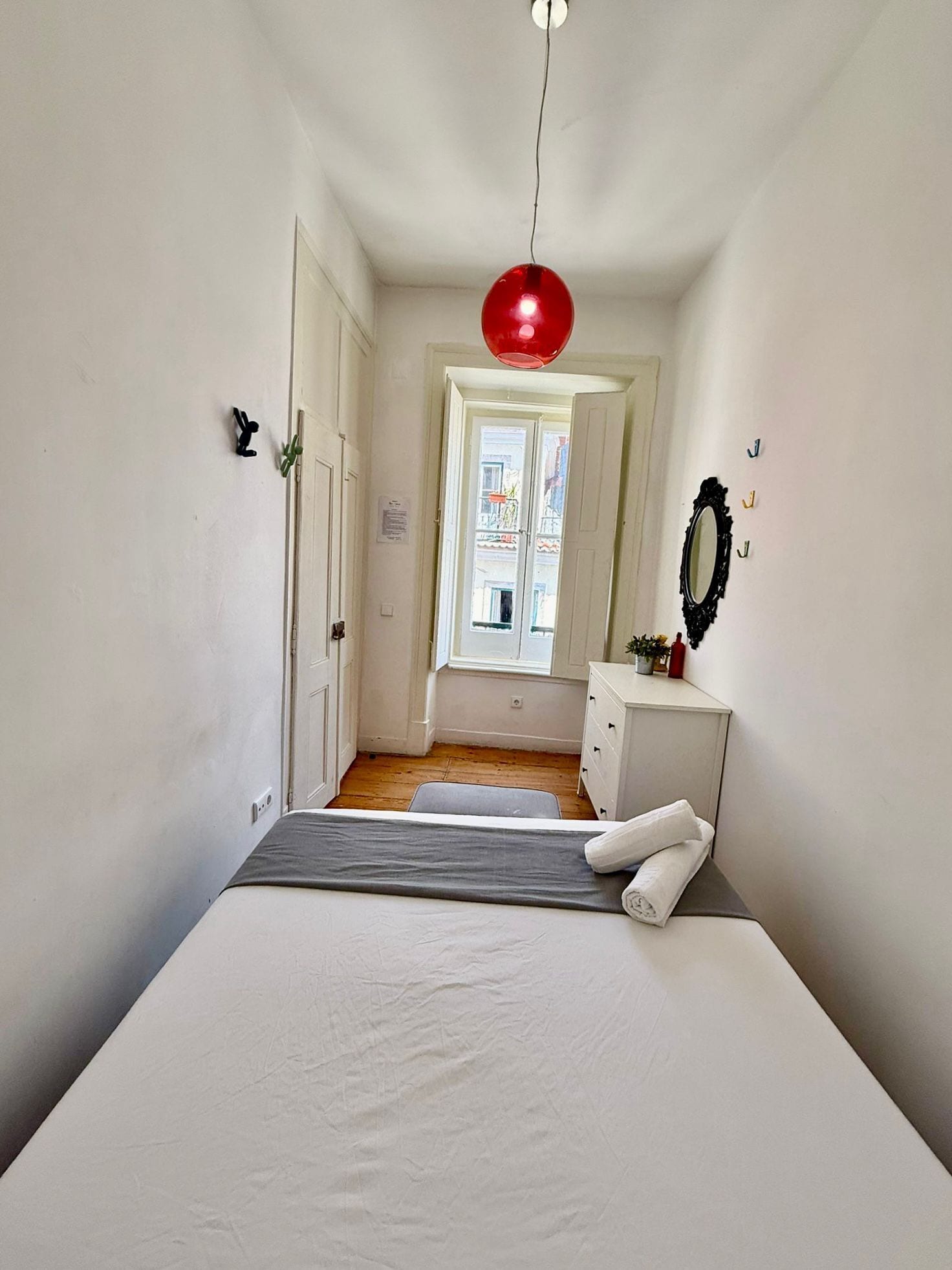 Une chambre à coucher avec un lit, une commode, une fenêtre et un luminaire suspendu rouge.