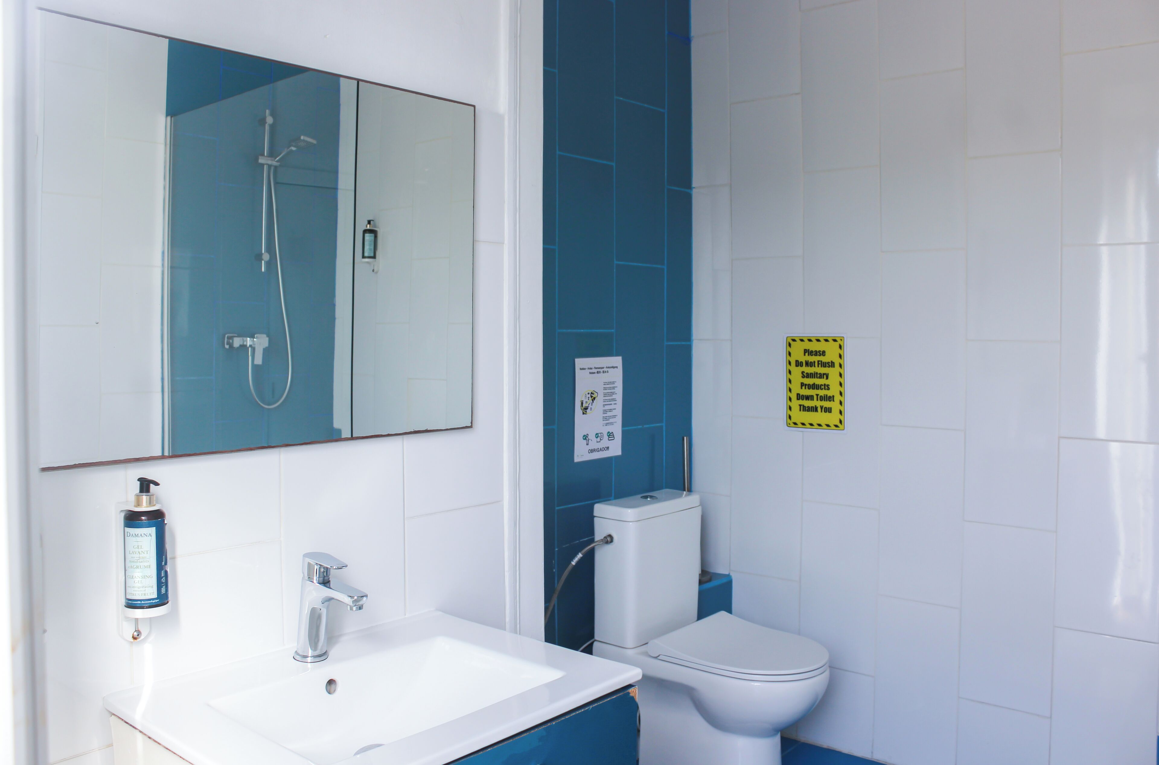 Baño con lavamanos blanco, espejo, ducha e inodoro.