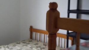 Une petite chambre avec un lit simple, une tête de lit en bois et un matelas recouvert d’un tissu à motifs.