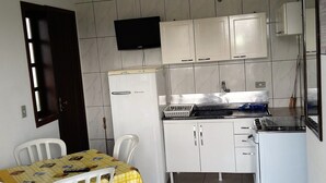 Une cuisine compacte avec des meubles blancs, un petit réfrigérateur, un four à micro-ondes et une cuisinière à gaz. Il y a une seule chaise et une table recouverte d’une nappe jaune.