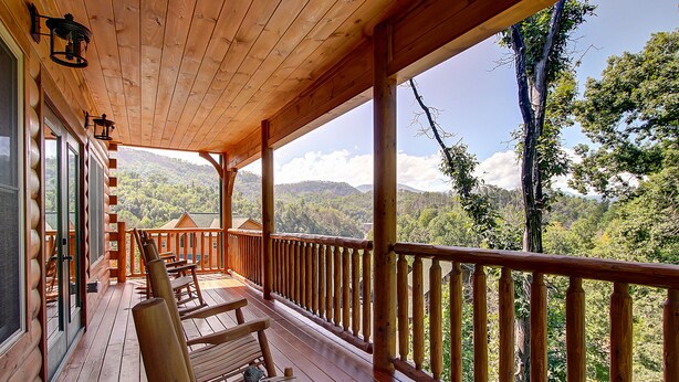 A wooden deck with benches and a railing overlooking a forested landscape. - Mountain view, sleeps 14, pool table, arcade game, and hot tub! Plenty of space! (Gatlinburg)