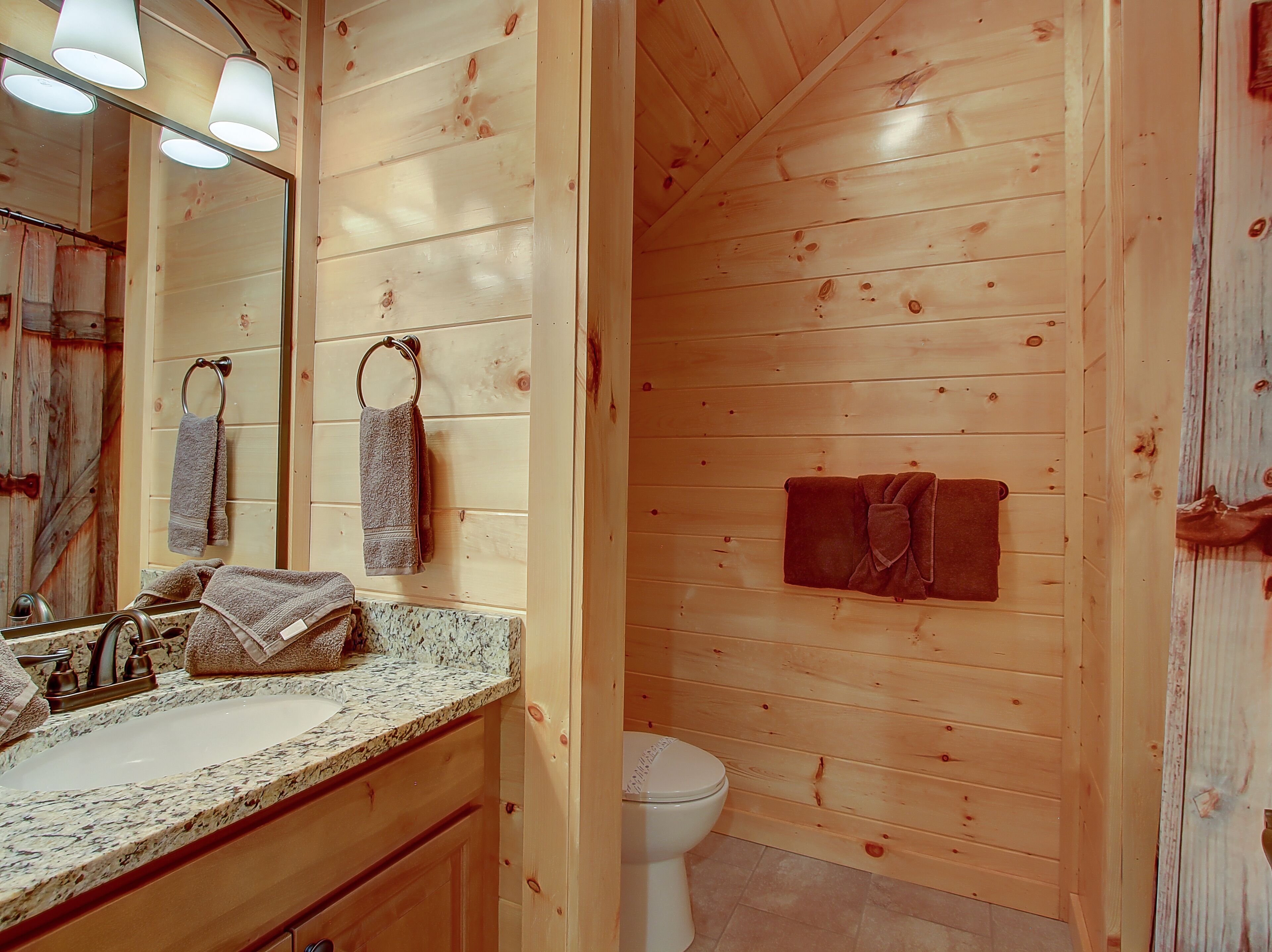 A wooden cabin bathroom with a granite countertop, a sink, a mirror, and a toilet.