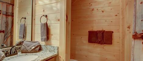 A wooden cabin bathroom with a granite countertop, a sink, a mirror, and a toilet.