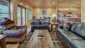 A cozy cabin interior with a living room, dining area, and kitchen. - Mountain view, sleeps 14, pool table, arcade game, and hot tub! Plenty of space! (Gatlinburg)