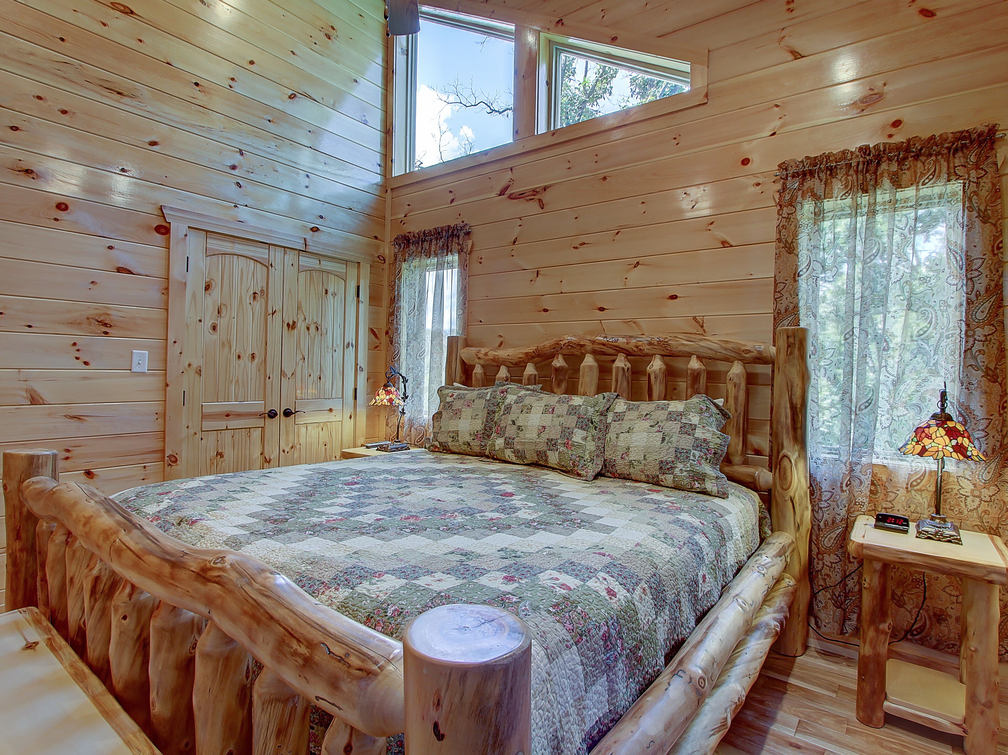Un dormitorio tipo cabaña de troncos con una cama grande, cabecera de madera y una mesita con lámpara.