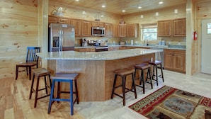 A spacious kitchen with wooden cabinets, a granite countertop, and a central island with stools. - Mountain view, sleeps 14, pool table, arcade game, and hot tub! Plenty of space! (Gatlinburg)