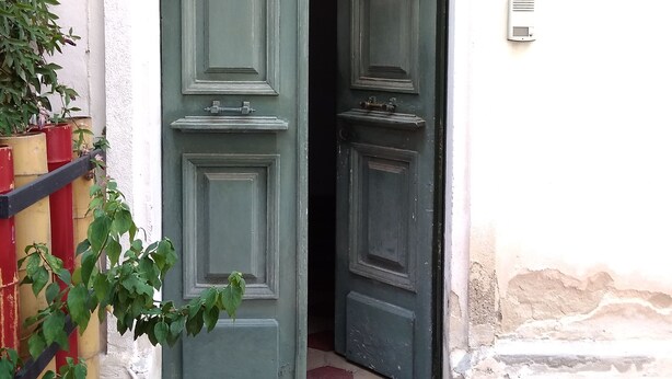 A green door with a small step leading up to it, a white wall, and a small white device on the wall. - Casa Diaz (Cagliari)