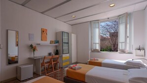 A hotel room with two beds, a desk, a chair, a small refrigerator, and a window with a view of trees. - Casa Diaz (Cagliari)