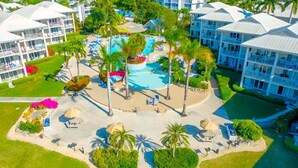Luftaufnahme eines Resorts mit mehreren Gebäuden, einem zentralen Poolbereich und umliegender Bepflanzung.