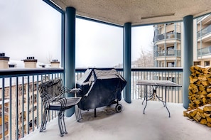A balcony with a grill, chairs, a table, and a stack of firewood.
