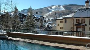 A pool area with a view of a mountain resort, including buildings and a ski slope. - Centennial 2 Bedroom Condo Unit no. 13ab (Avon)