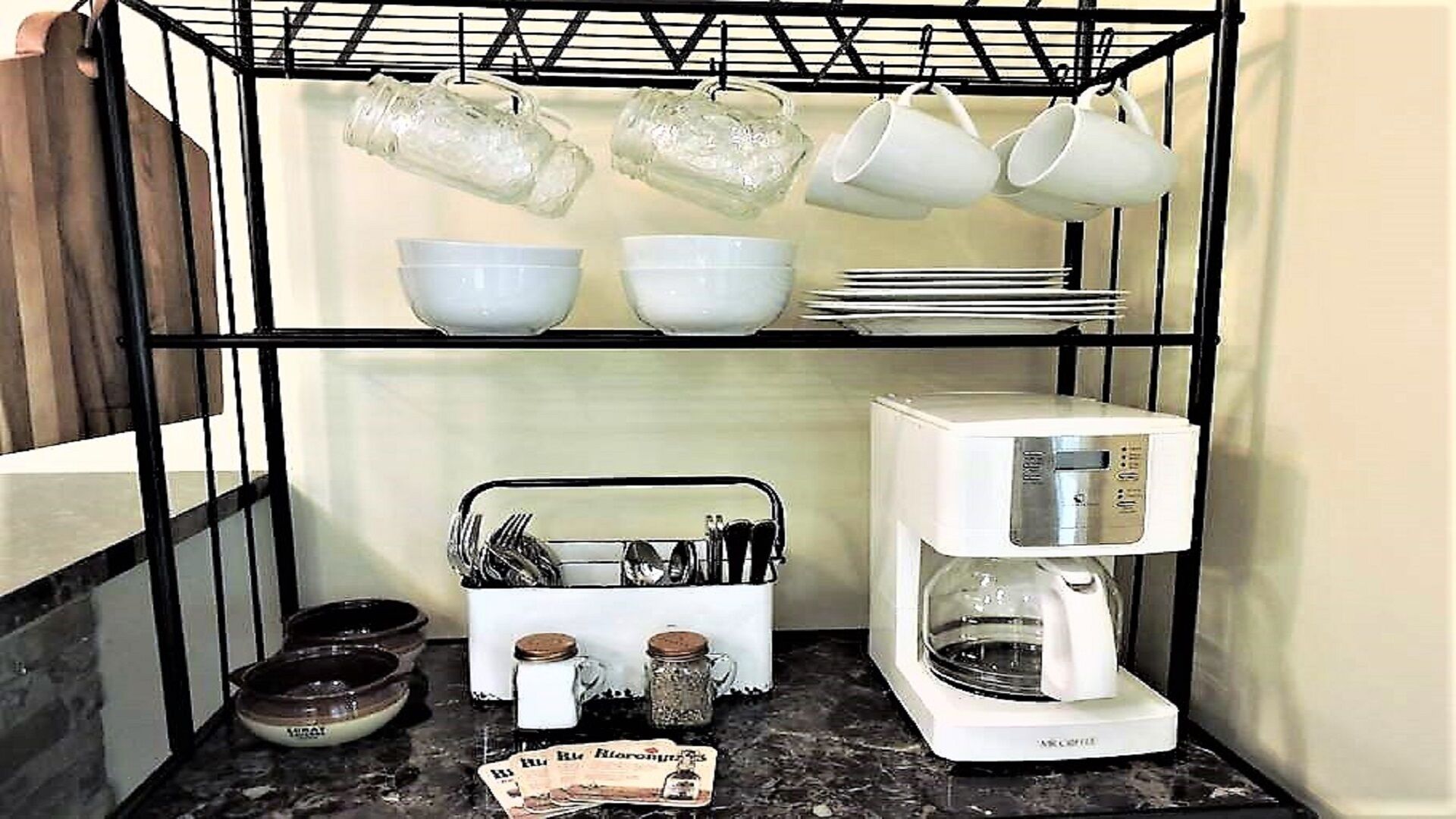 A kitchen with a coffee maker, bowls, cups, and utensils on shelves.