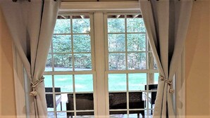 A large window with white frames and curtains tied back, revealing a view of a lawn and outdoor seating area.